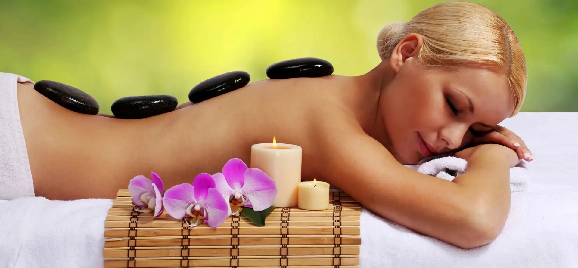 A woman laying on bamboo mat with candles and flowers.